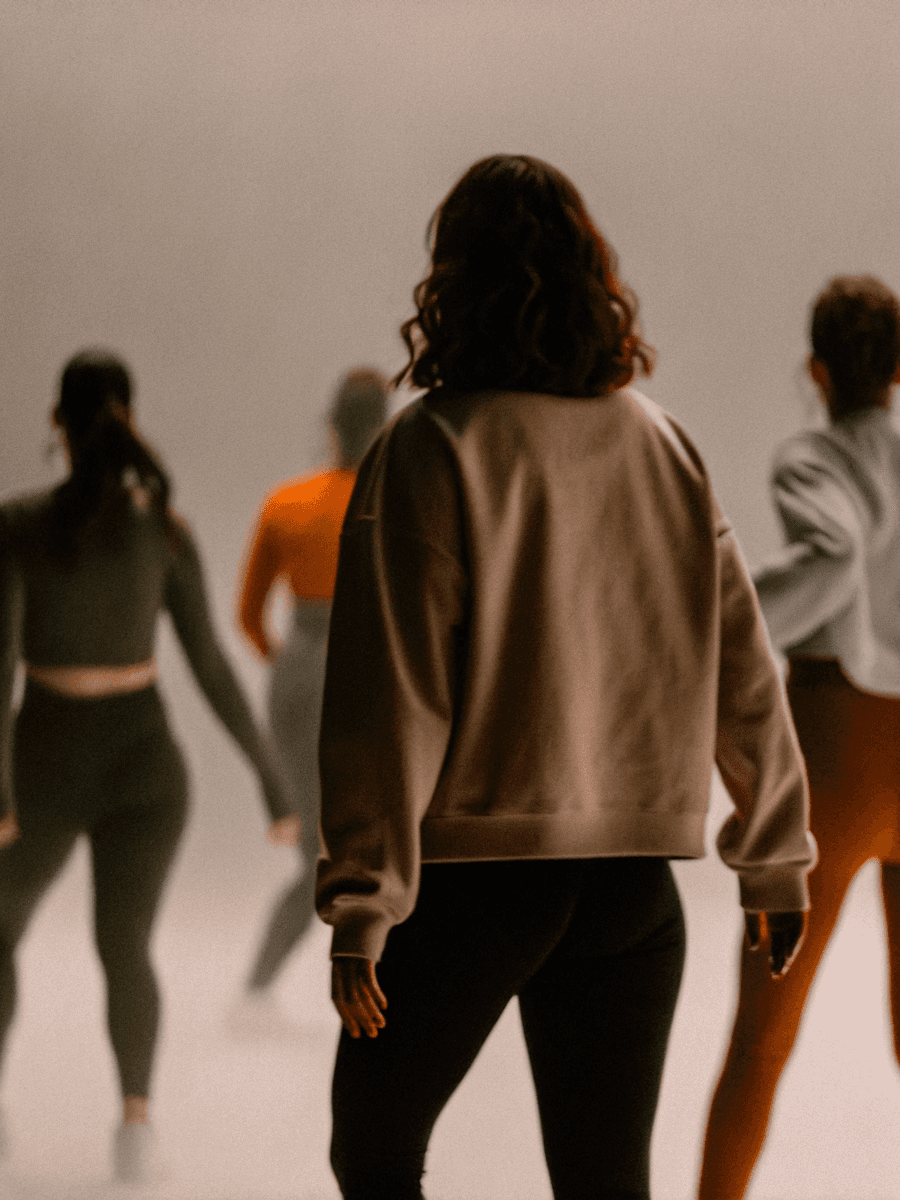 Woman in sweatshirt faces away during group fitness class session.