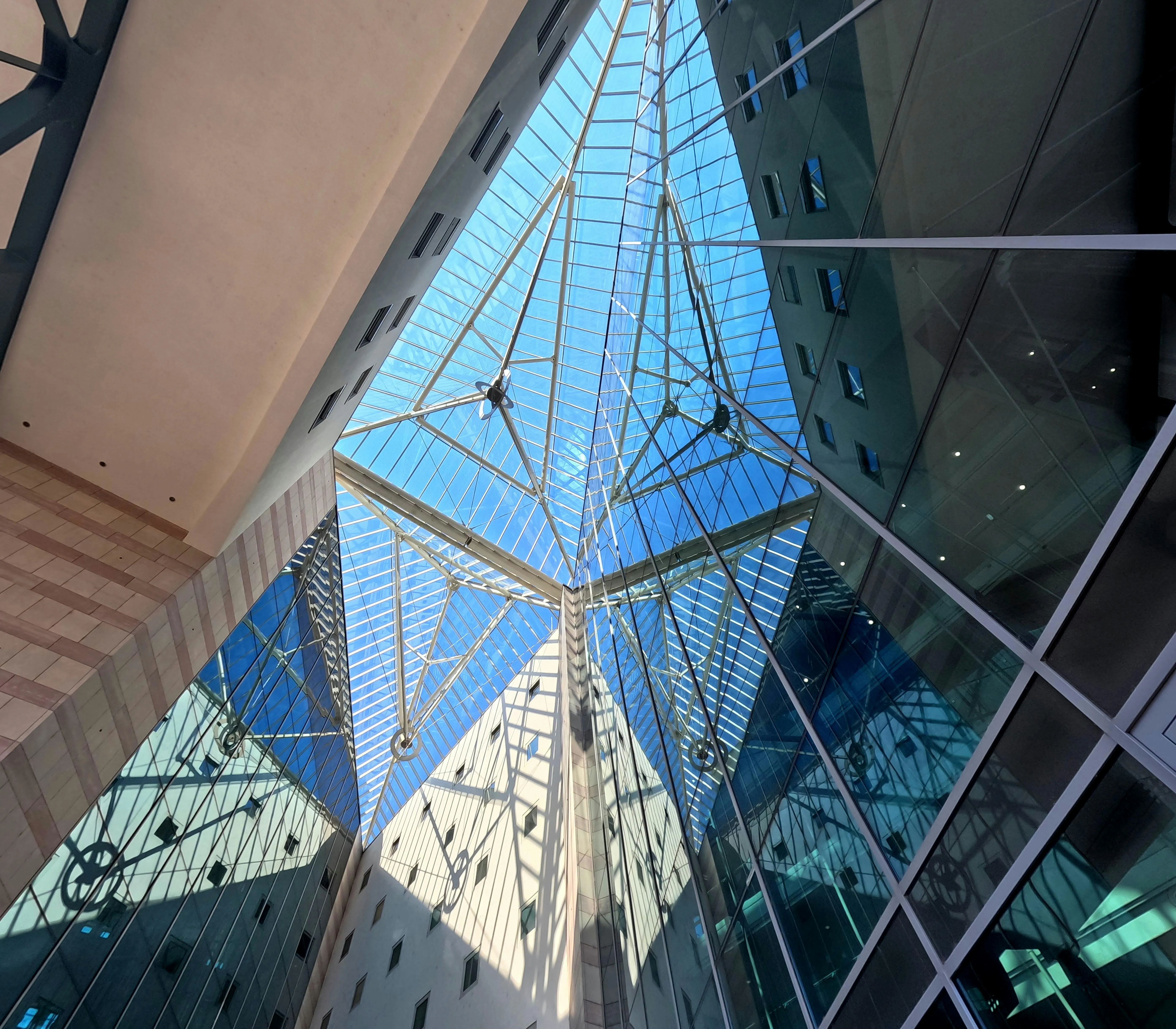 Low-angle view of a contemporary glass atrium with a massive triangular skylight reflecting the blue sky.