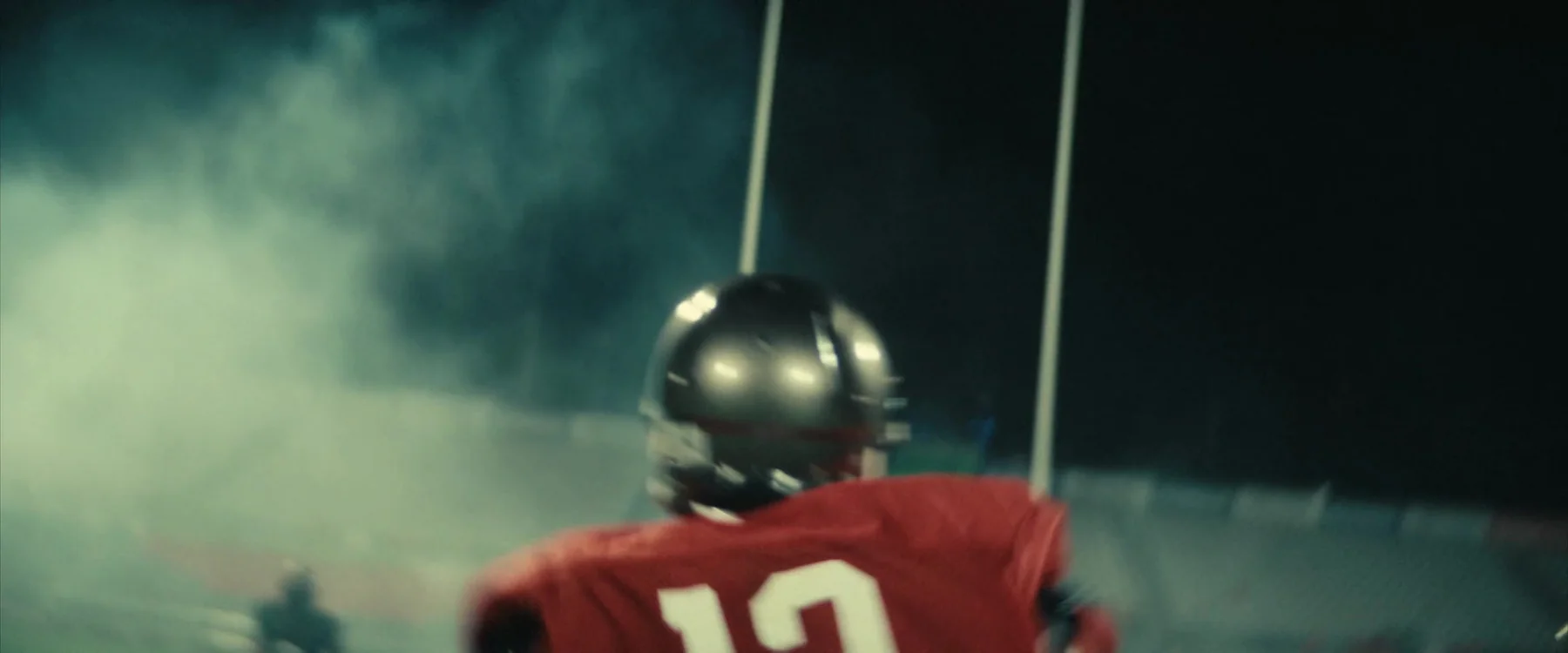  Football players running through a fog-filled tunnel toward the field at night