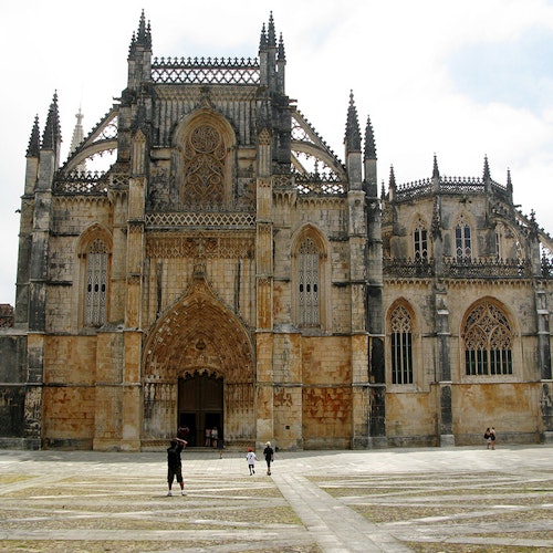 يتجه الناس نحو كاتدرائية قوطية كبيرة مزخرفة ذات أقواس مدببة ونقوش حجرية مفصلة في يوم غائم.