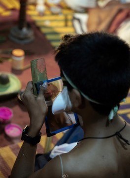 A Kathakali performer checking his half-finished makeup in a hand mirror