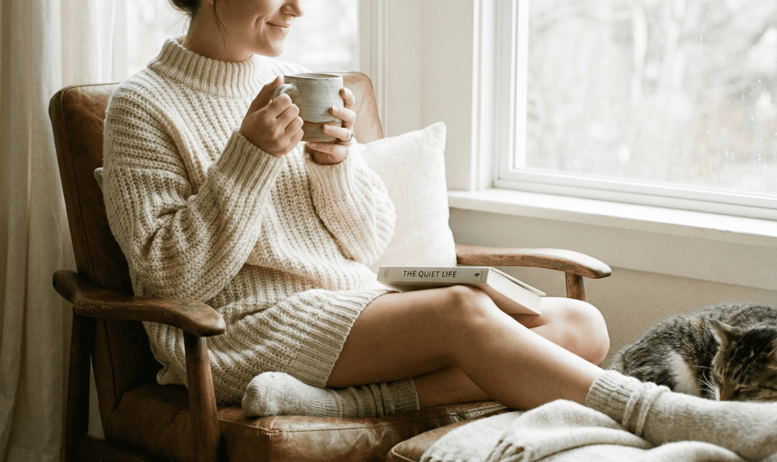 Person relaxing in a chair holding a warm mug of coffee with both hands, reading a book