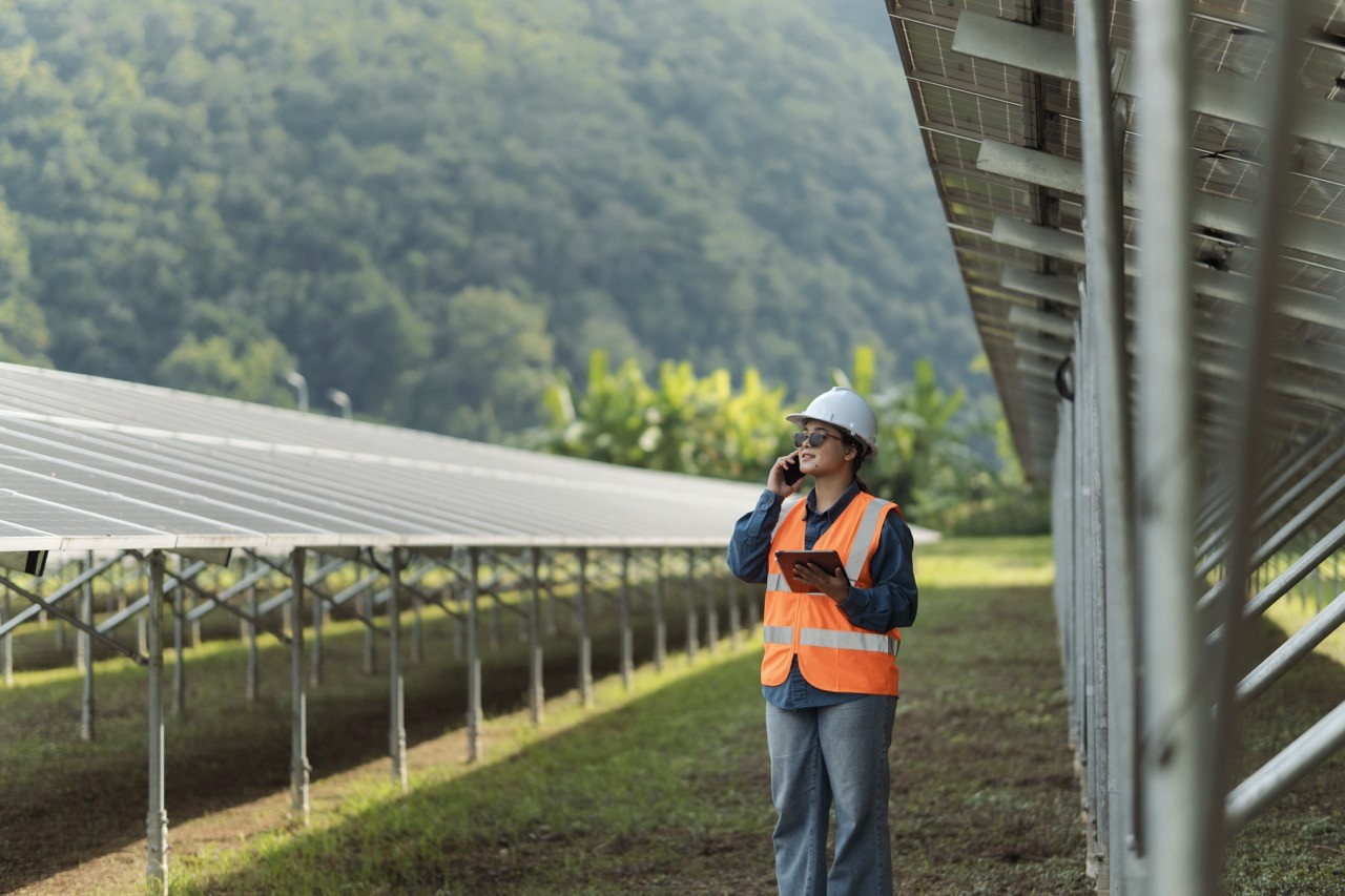 Site personnel between two rows of solar panels in a field on an ipad and phone call