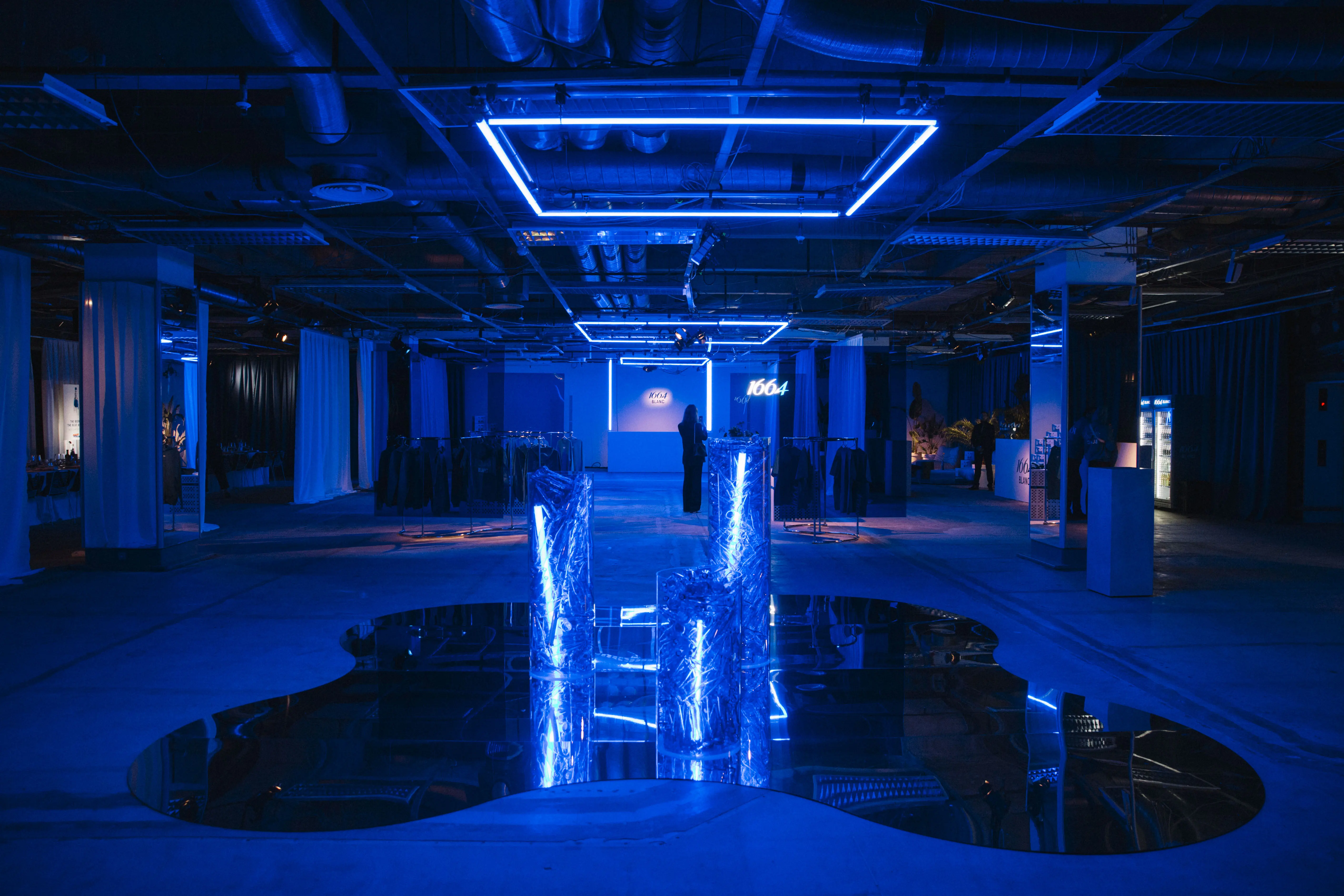 Blue-lit event space with neon ceiling frames, glowing ice pillars and mirrored floor pool.