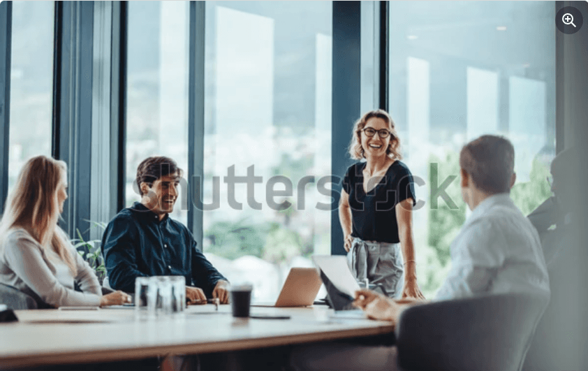 Woman in blue hat and sweater sitting on couch with laptop.