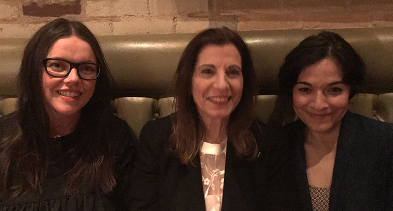 A photo of three women sitting on a leather sofa.