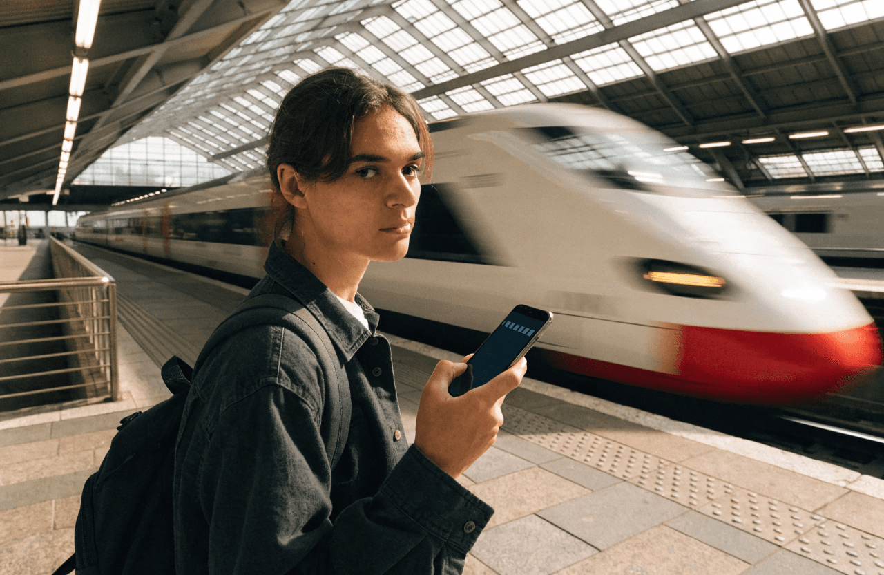 Persona joven usando el móvil con cobertura en una estación con un tren de alta velocidad
