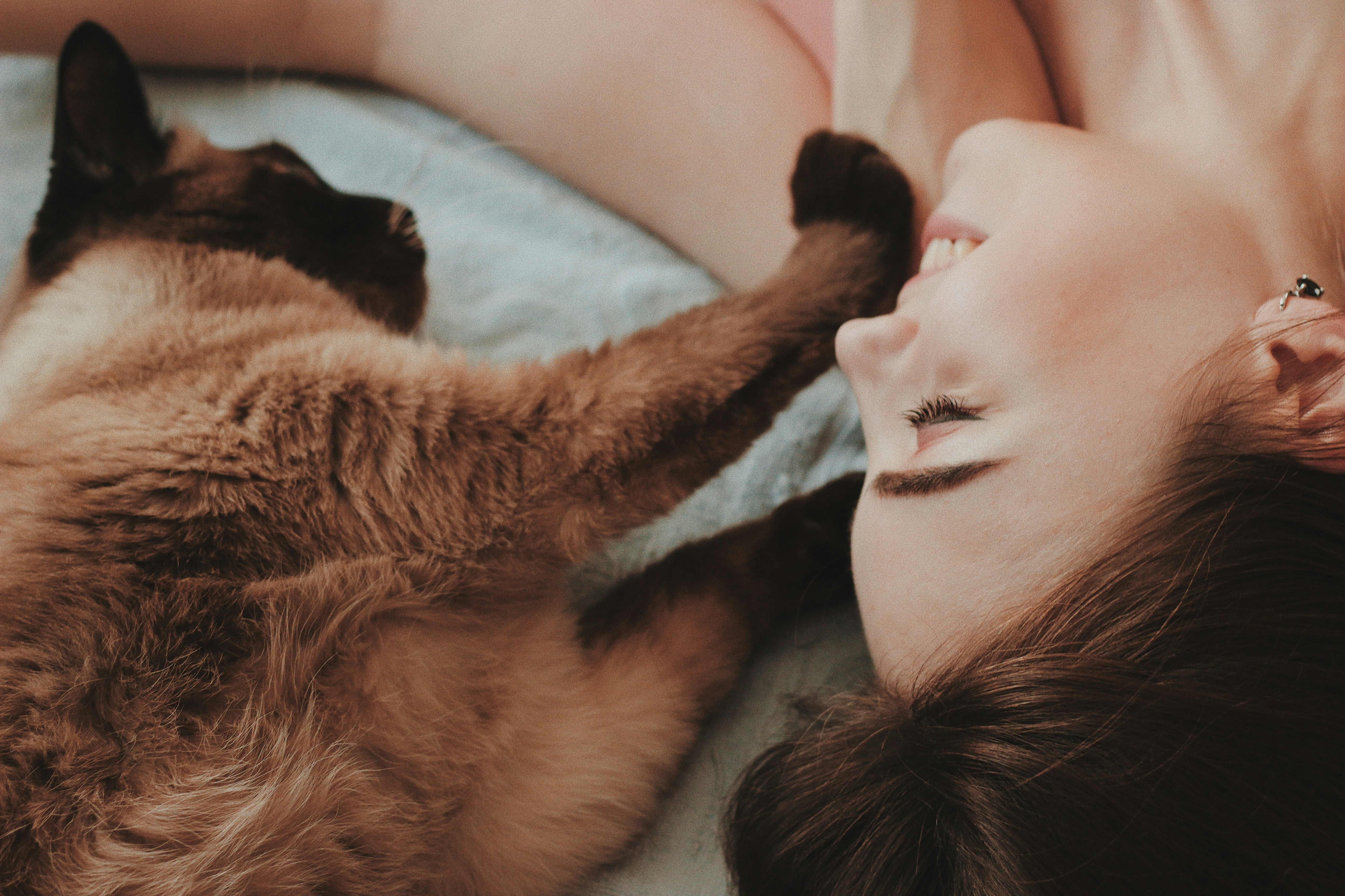 A woman on bed being gently touched in the face by a cat's paws