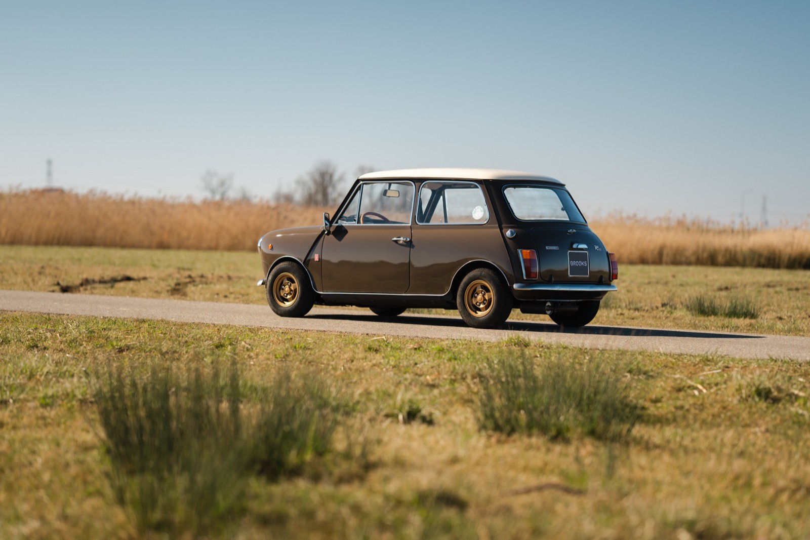 A vintage car parked on a dirt road, surrounded by grassy fields and a clear blue sky.