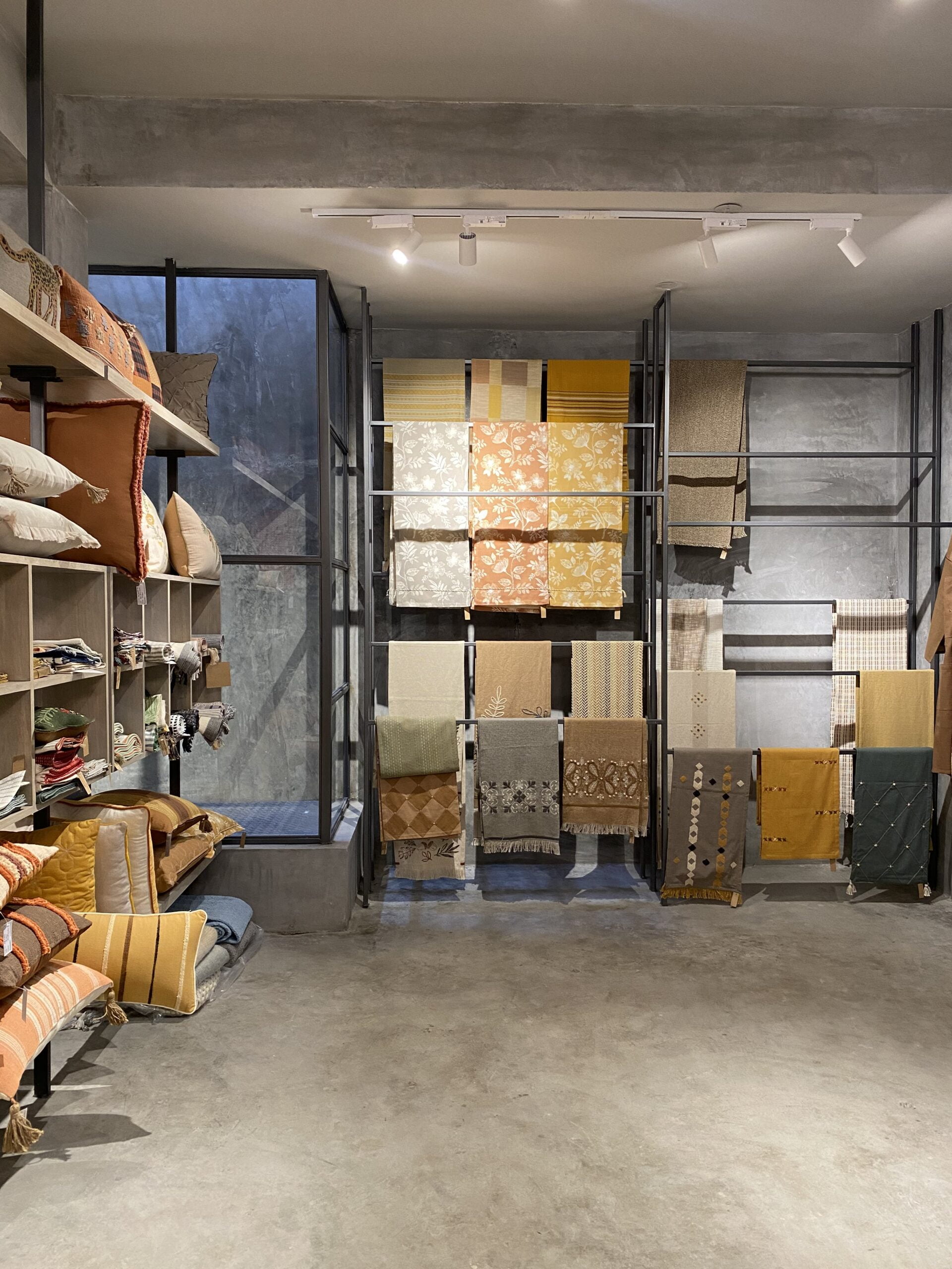 Texture and tone: A curated retail space where the softness of cushions and throws contrasts effectively with the rugged, grey-toned industrial shell.