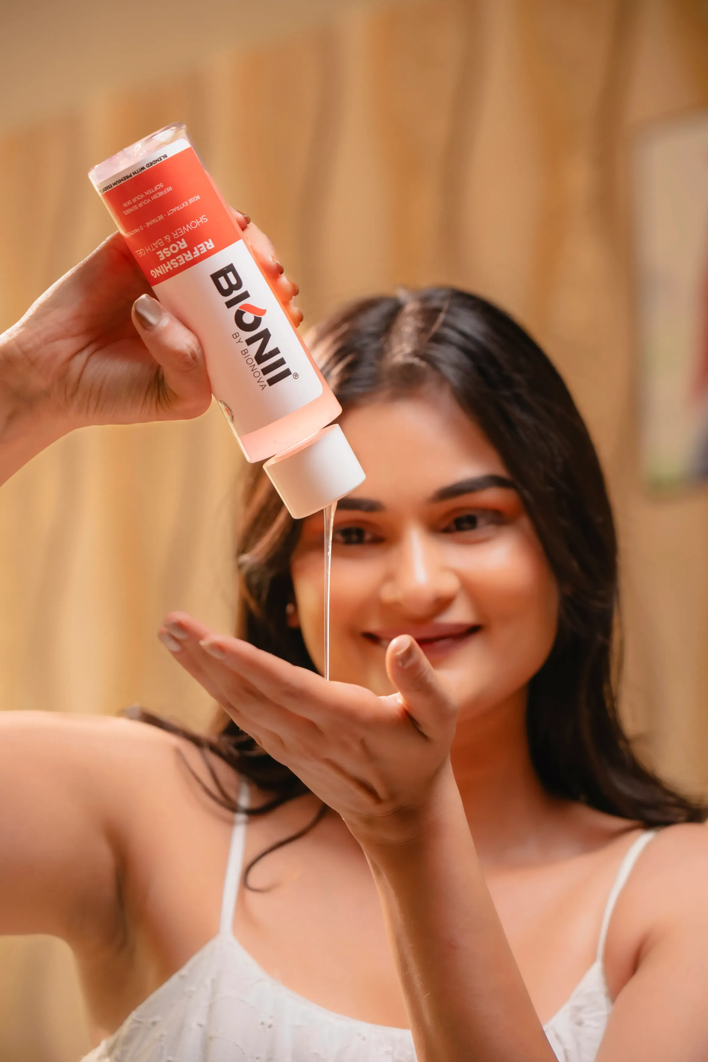 A woman smiling while dispensing a product from a bottle into her palm. She has long, dark hair.