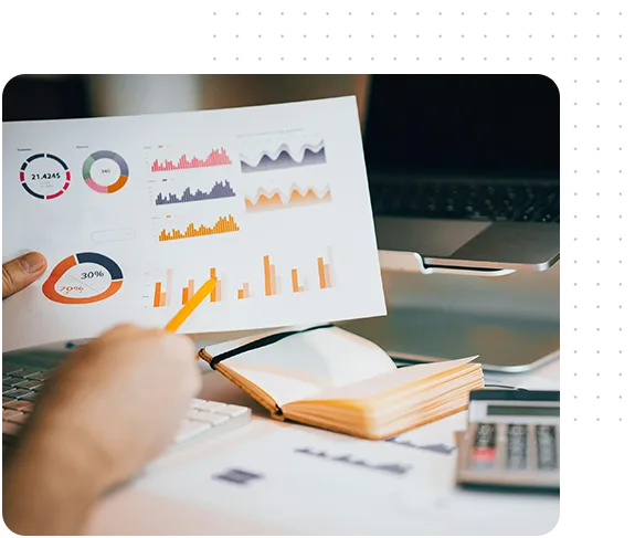 A person holding a paper with colorful logos and sketches, sitting at a table with a calculator and materials.