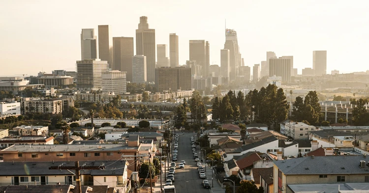 Uma vista panorâmica do centro de Los Angeles, apresentando um horizonte de modernos edifícios altos sob um céu claro e ensolarado, com bairros residenciais e ruas arborizadas em primeiro plano, capturando a paisagem urbana da cidade.