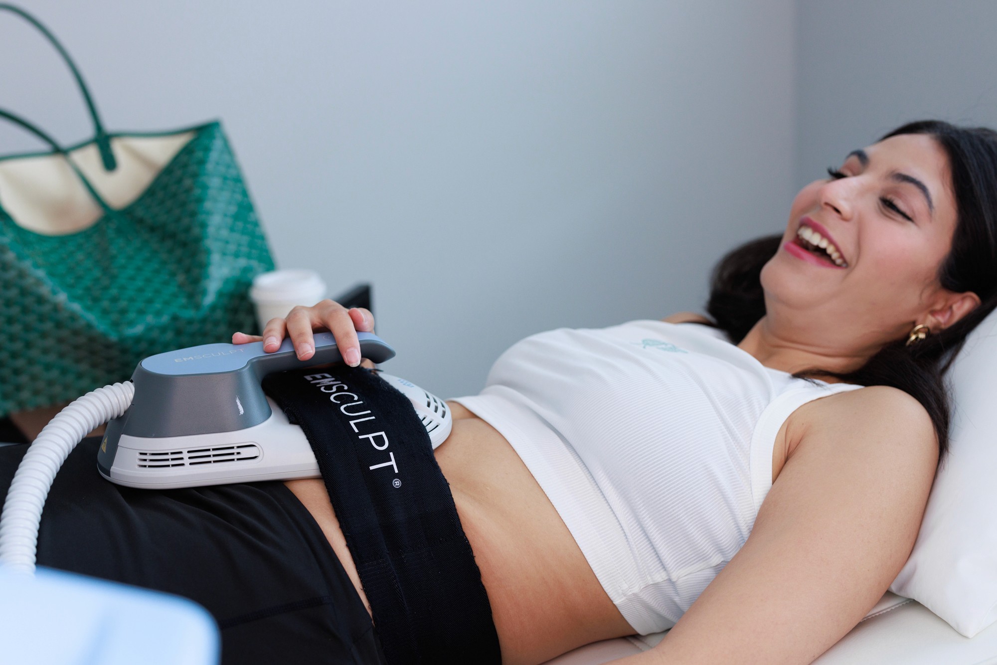 Smiling patient lying down receiving an EmSculpt treatment on the abdomen.