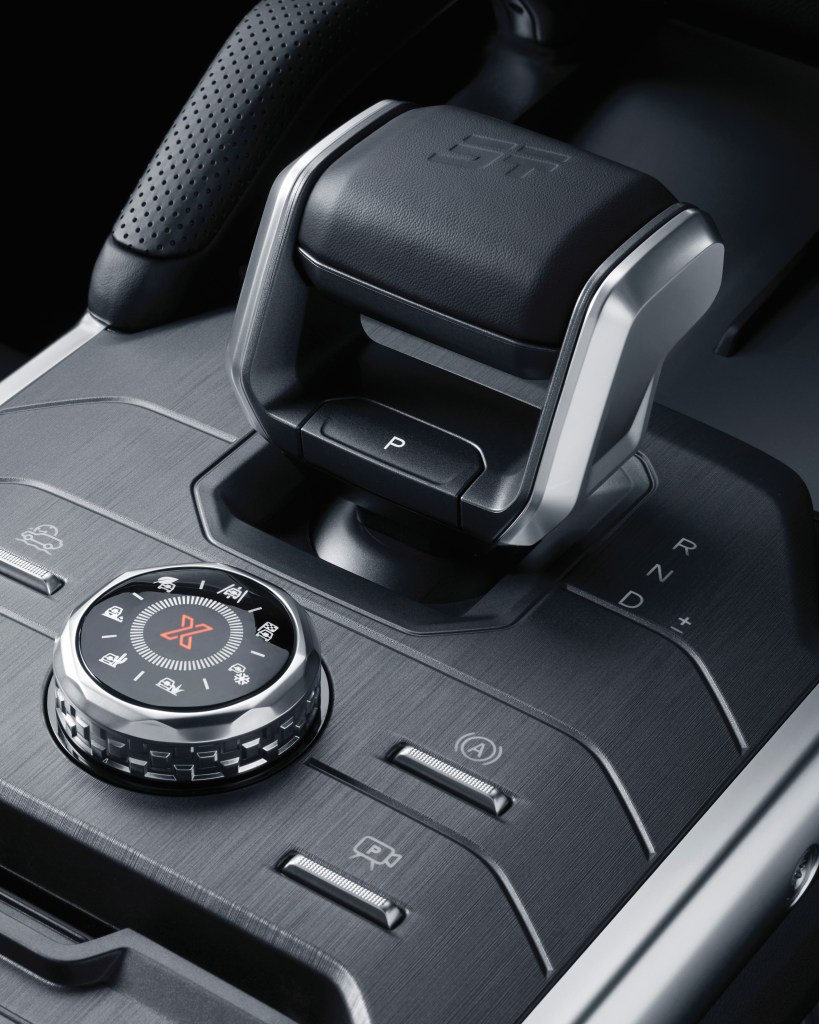 Close-up view of a car's gear shift and control dials on the center console, featuring a sleek design with metallic and textured elements.