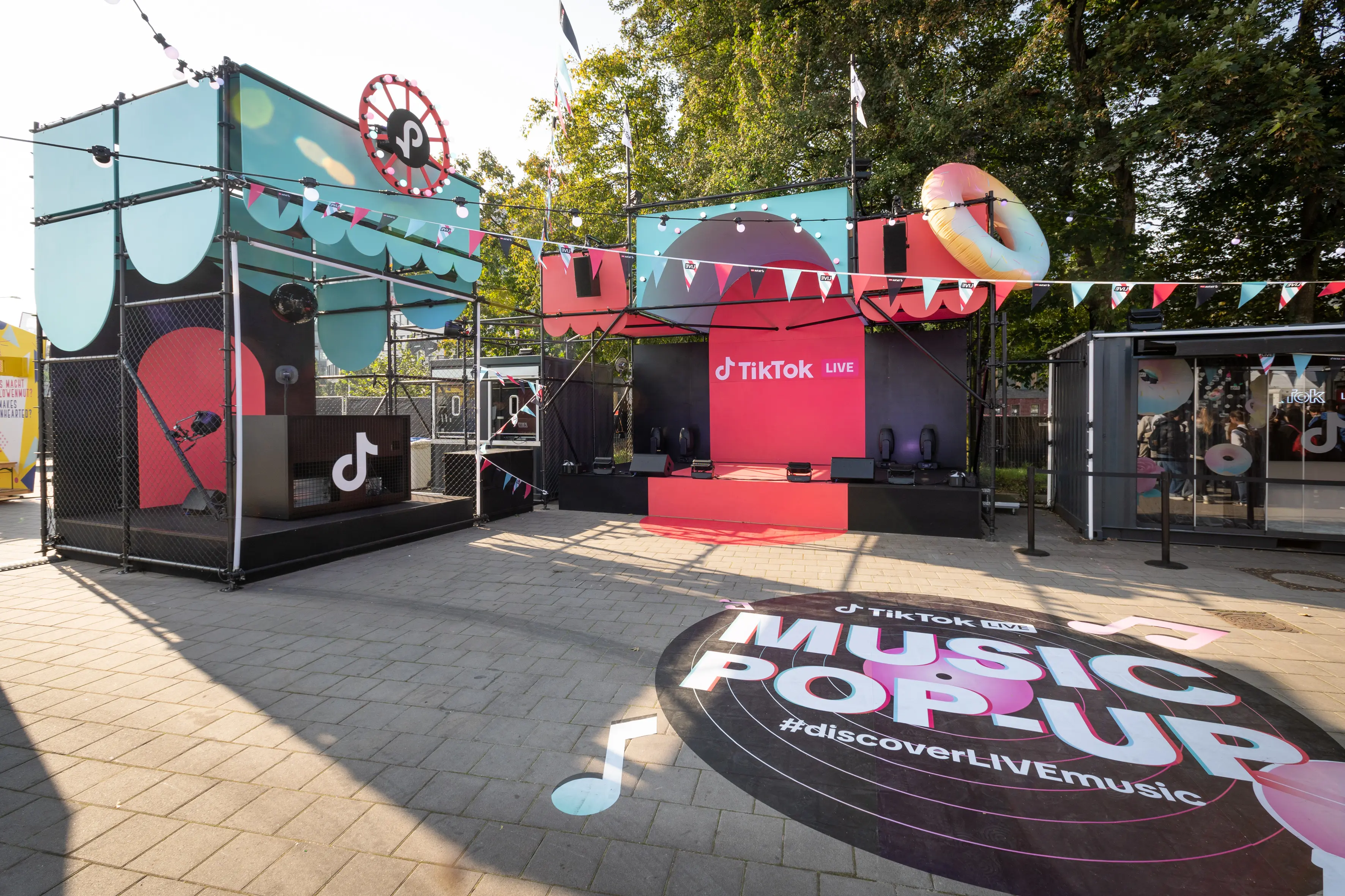 TikTok Live music pop-up with red stage, scaffold cubes, donut float and bunting in daylight.