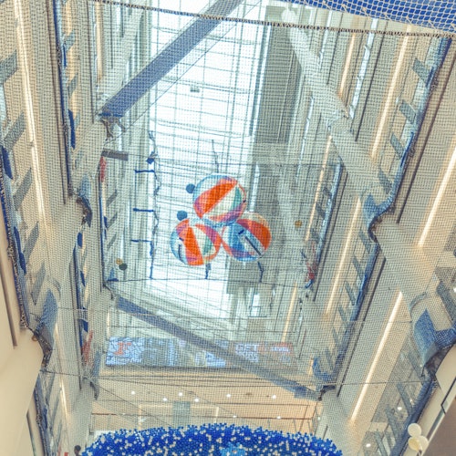 View of a high ceiling inside a building, featuring a net holding colorful beach balls and an arrangement of blue and white decorations.