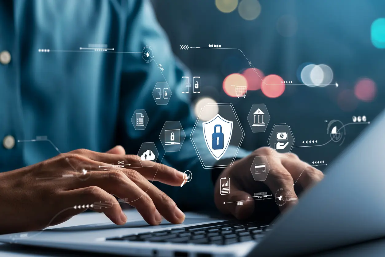 Hands typing on a laptop surrounded by holographic cybersecurity icons, illustrating critical infrastructure protection against insider threats