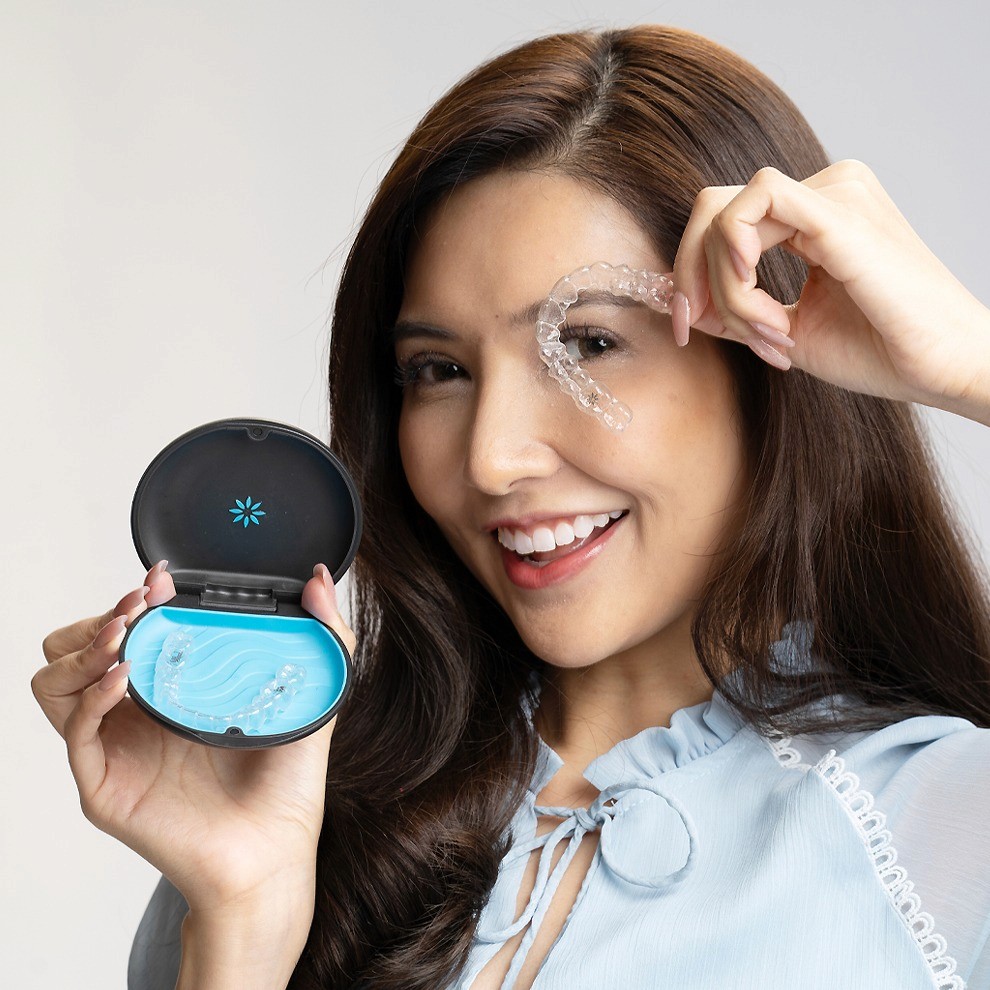 A woman smiles and holds invisalign clear aligners with a case, showcasing a certified invisalign provider at Bella Medical Centre