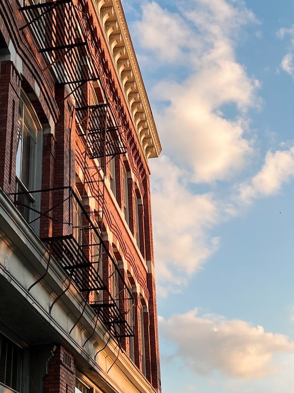 Red brick building with fire escape against blue sky - classic urban architecture with ornate cornice detail