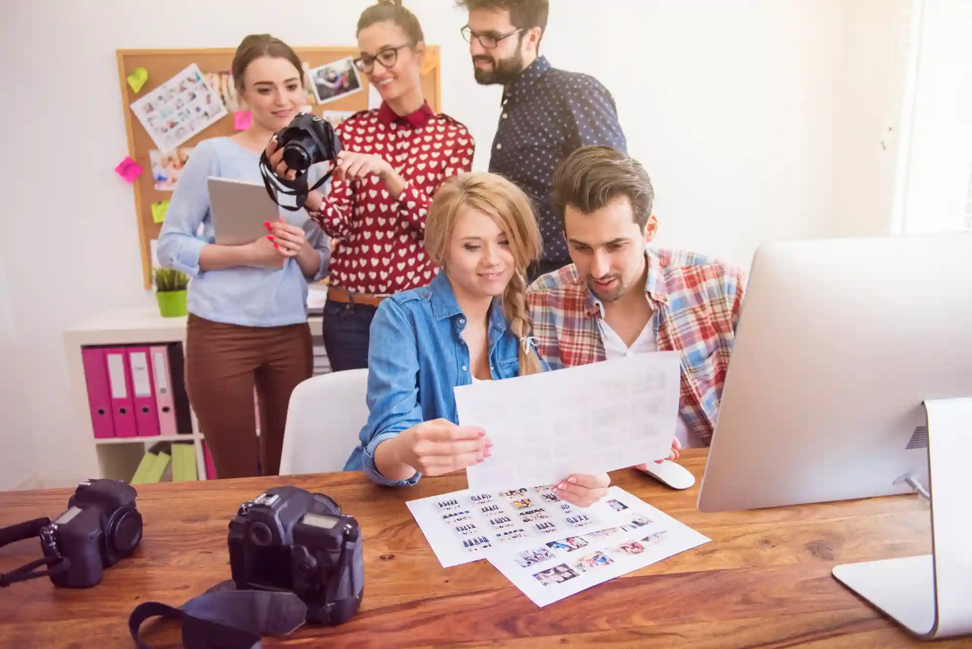 A collaborative creative team reviews printed visual assets and photography equipment while working together in a modern office.
