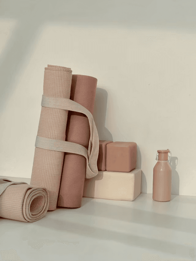 Minimalist setup of rolled-up pink yoga mats with matching blocks and a ceramic vase.