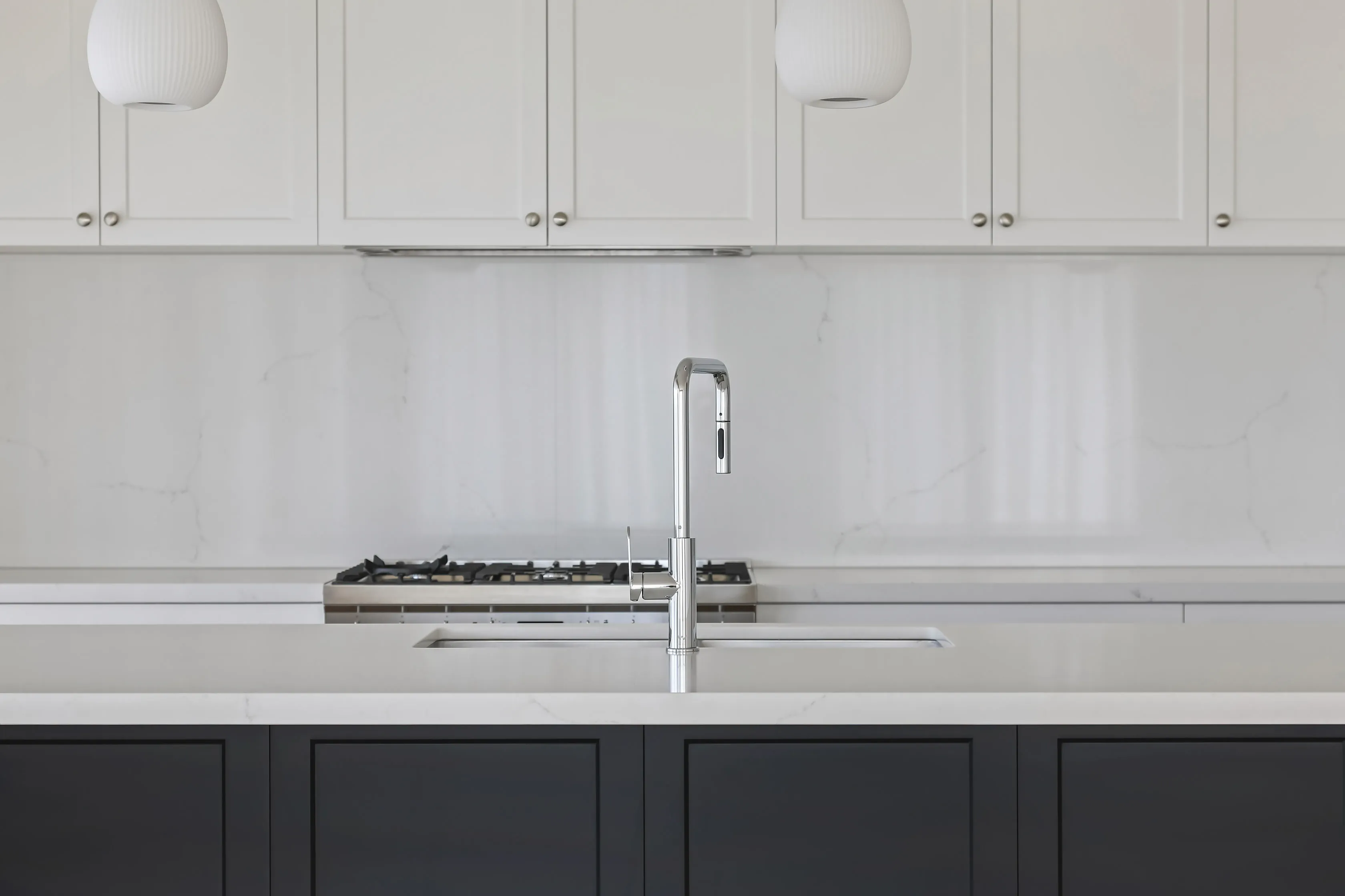 Kitchen detail with two ribbed-glass pendant lights, white shaker overhead cabinets, a marble-look splashback, gas cooktop and a chrome pull-down tap over an undermount sink in the charcoal island