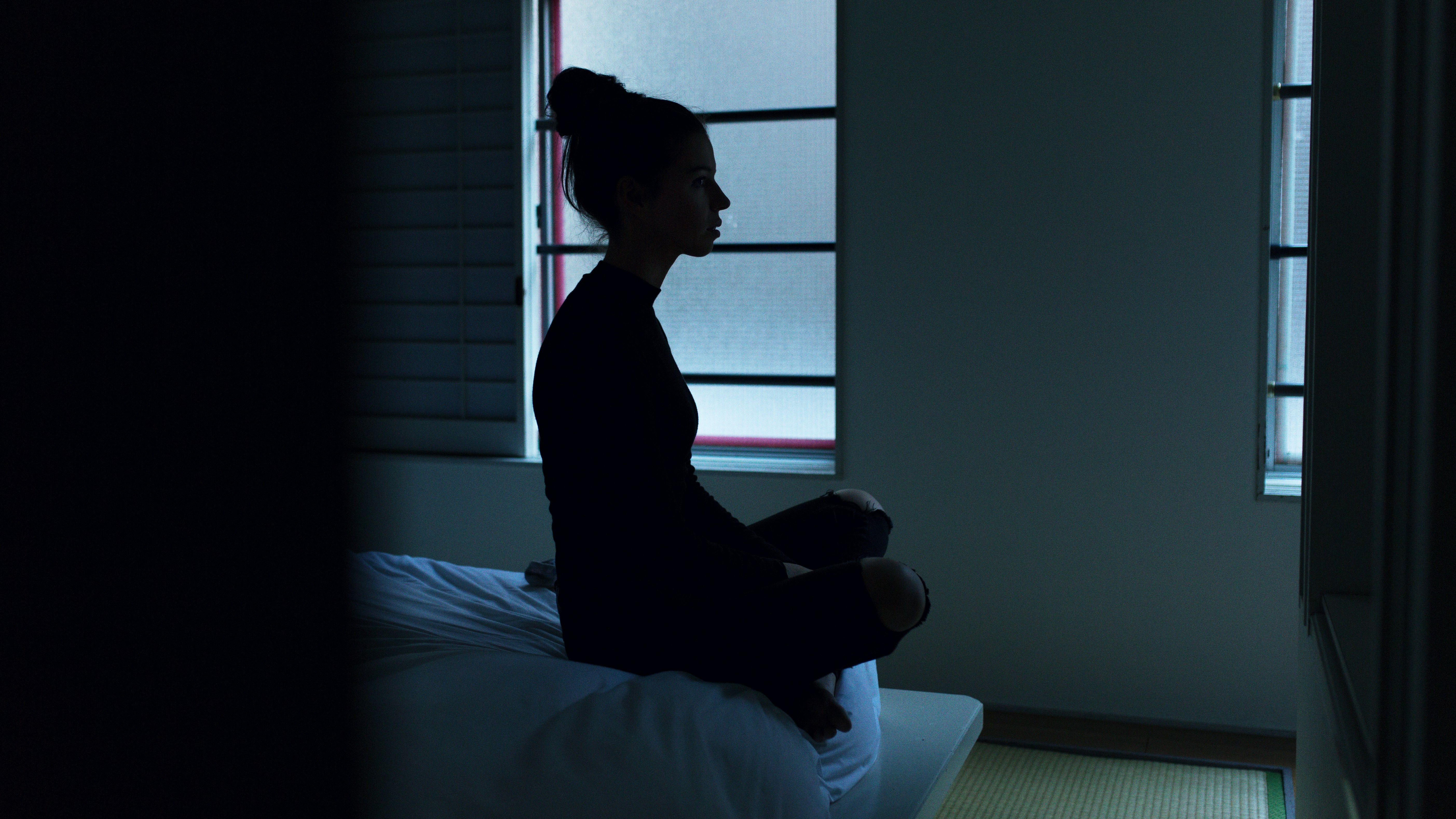 Woman sitting cross-legged on the edge of the bed in darkness