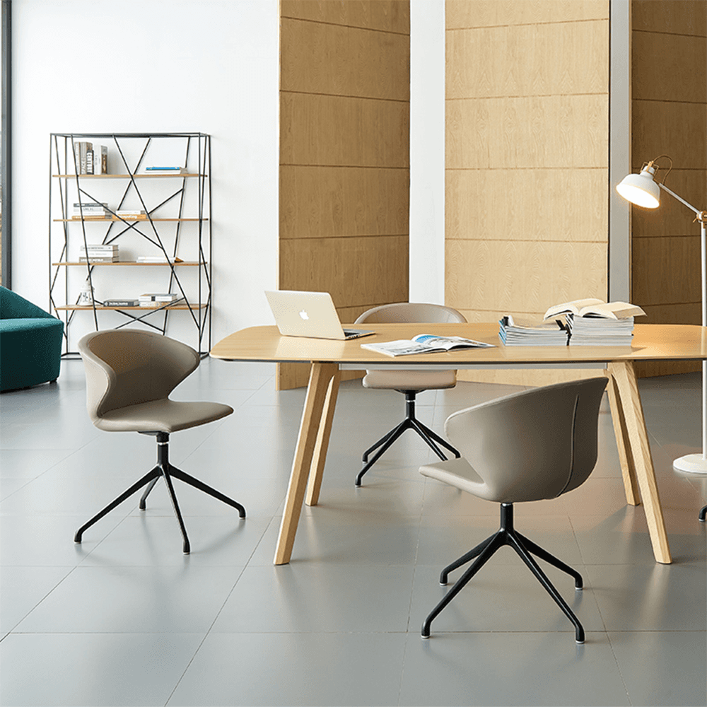 Three modern taupe leather swivel chairs arranged around a light wood conference table in a bright, minimalist office space featuring a geometric bookshelf and natural wood partitions.