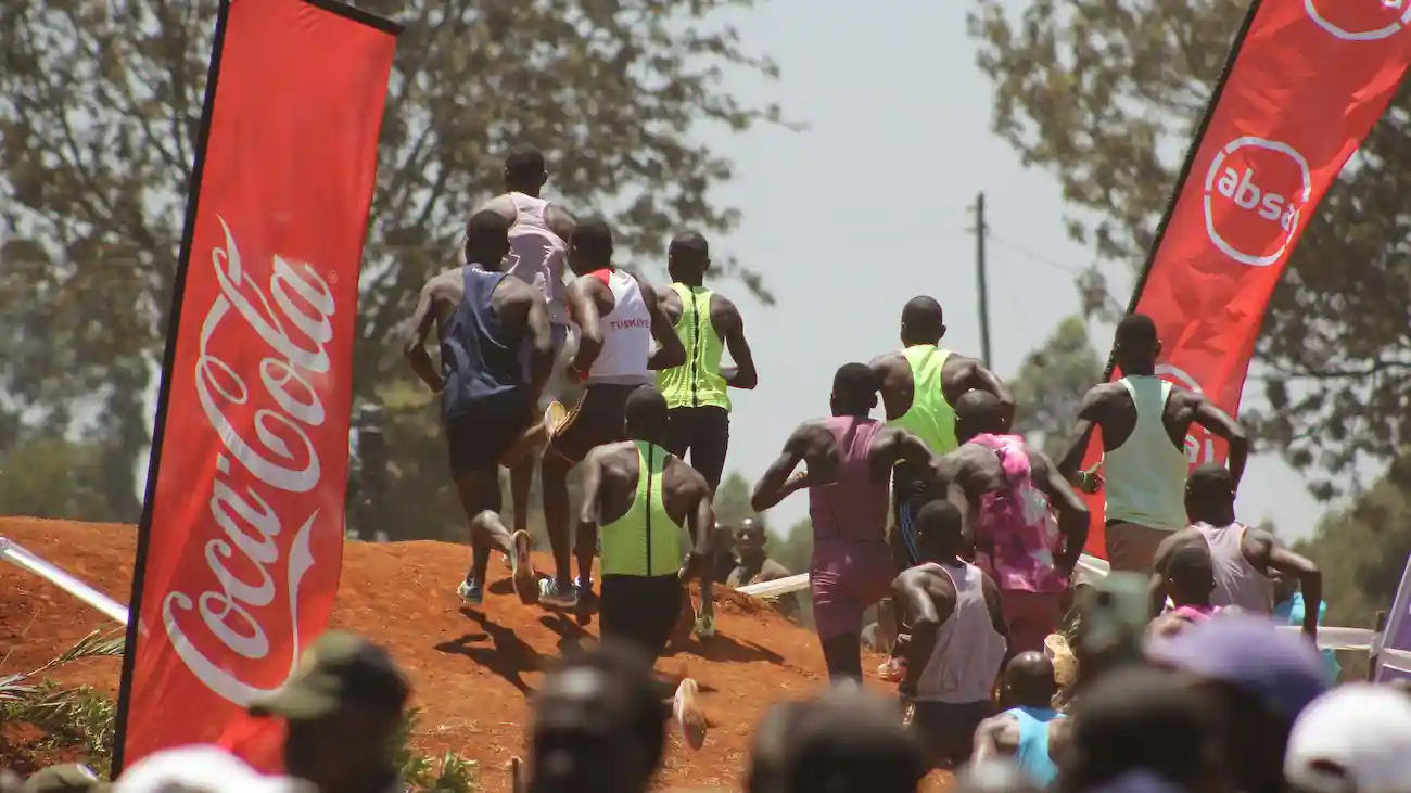 Runners compete in a road race between branded flags and sponsor banners — illustrating sports sponsorship and how brands use event visibility and community engagement.