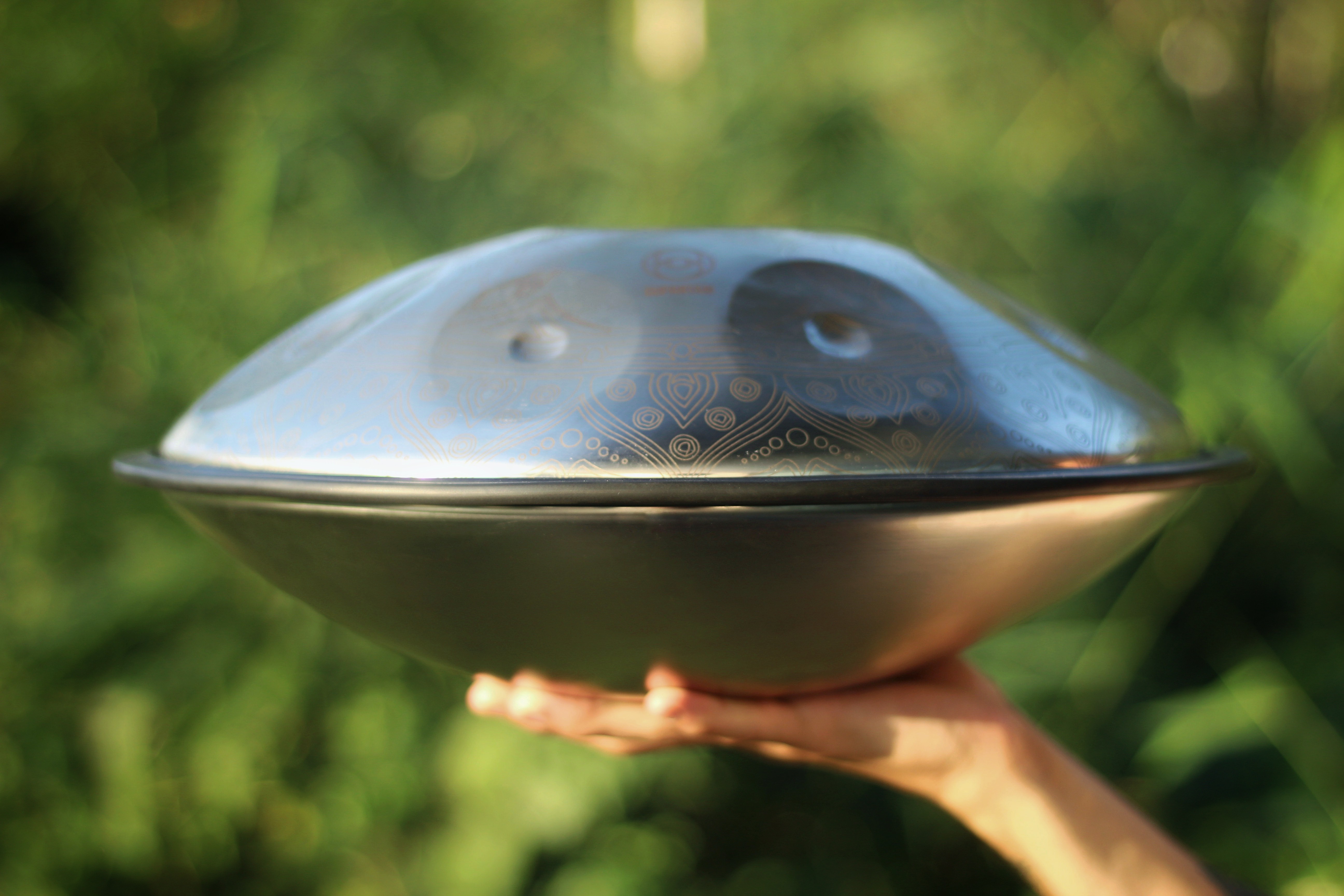 Someone holding a travel-sized handpan in the air, displaying a side view.