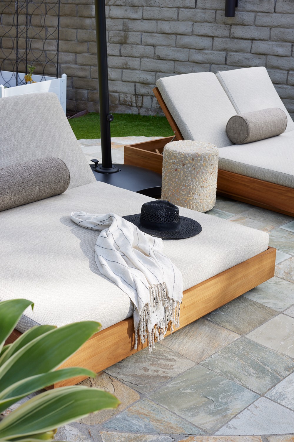 Sun beds with linen upholstery and accent pillows, complemented by stone, wood, and metal accents, create an elegant seating arrangement