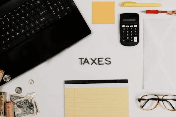 Office desk with 'TAXES' spelled out, calculator, cash, and notebook, symbolizing tax reduction strategies for corporate law firms.