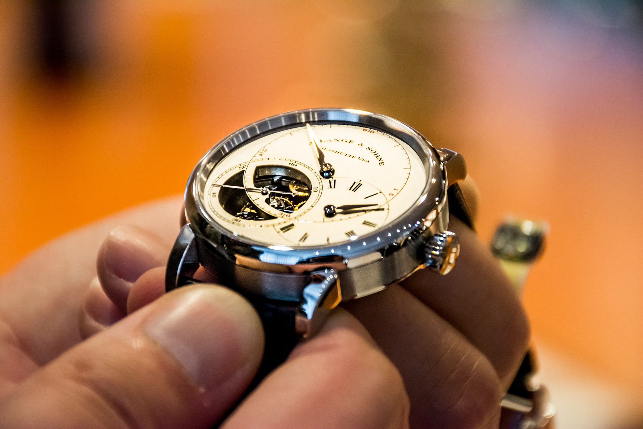 A person's hand holding a silver and black chronograph watch with a white face and gold accents.