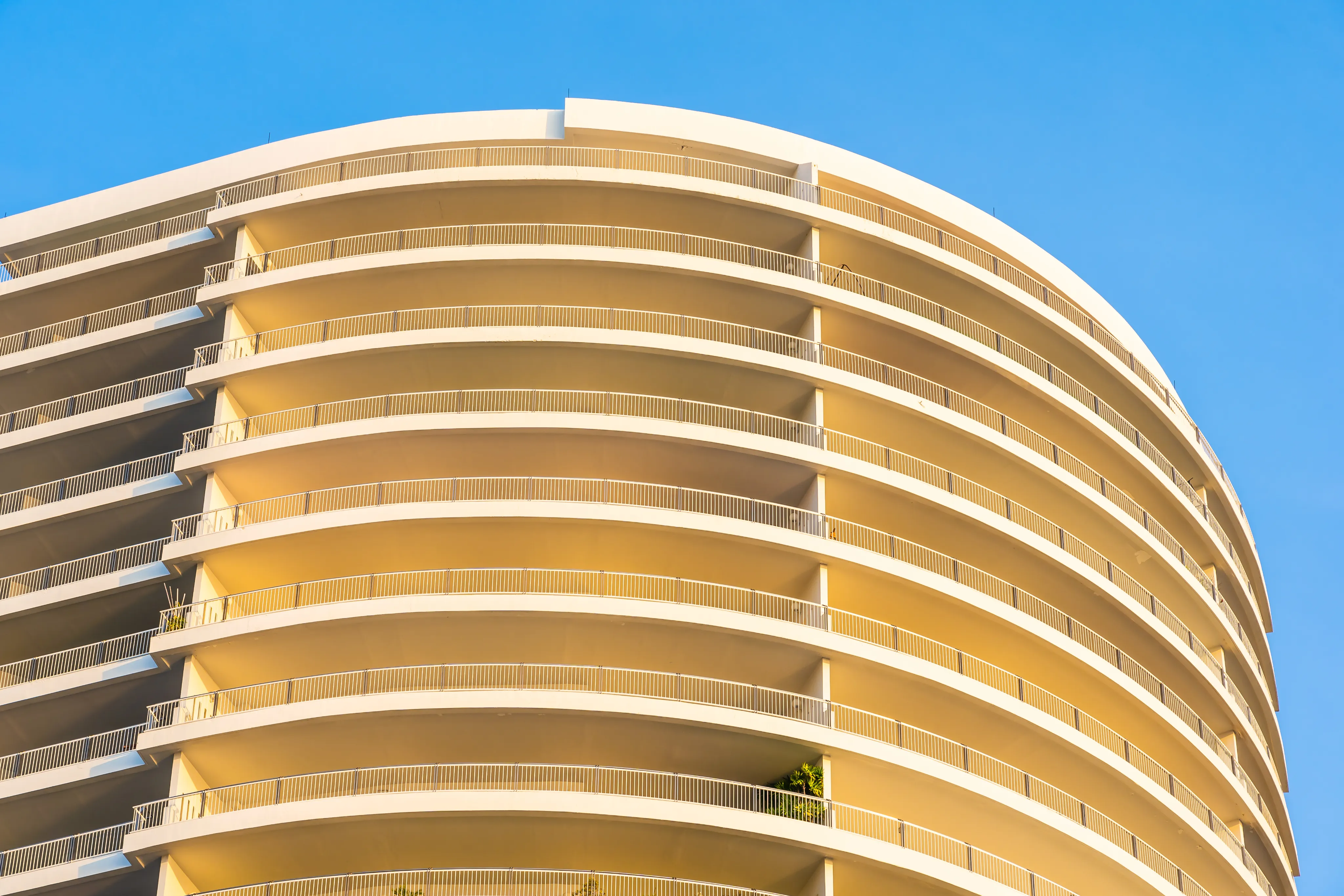 Low-angle view of a contemporary white high-rise residential building with curved balconies against a clear blue sky.