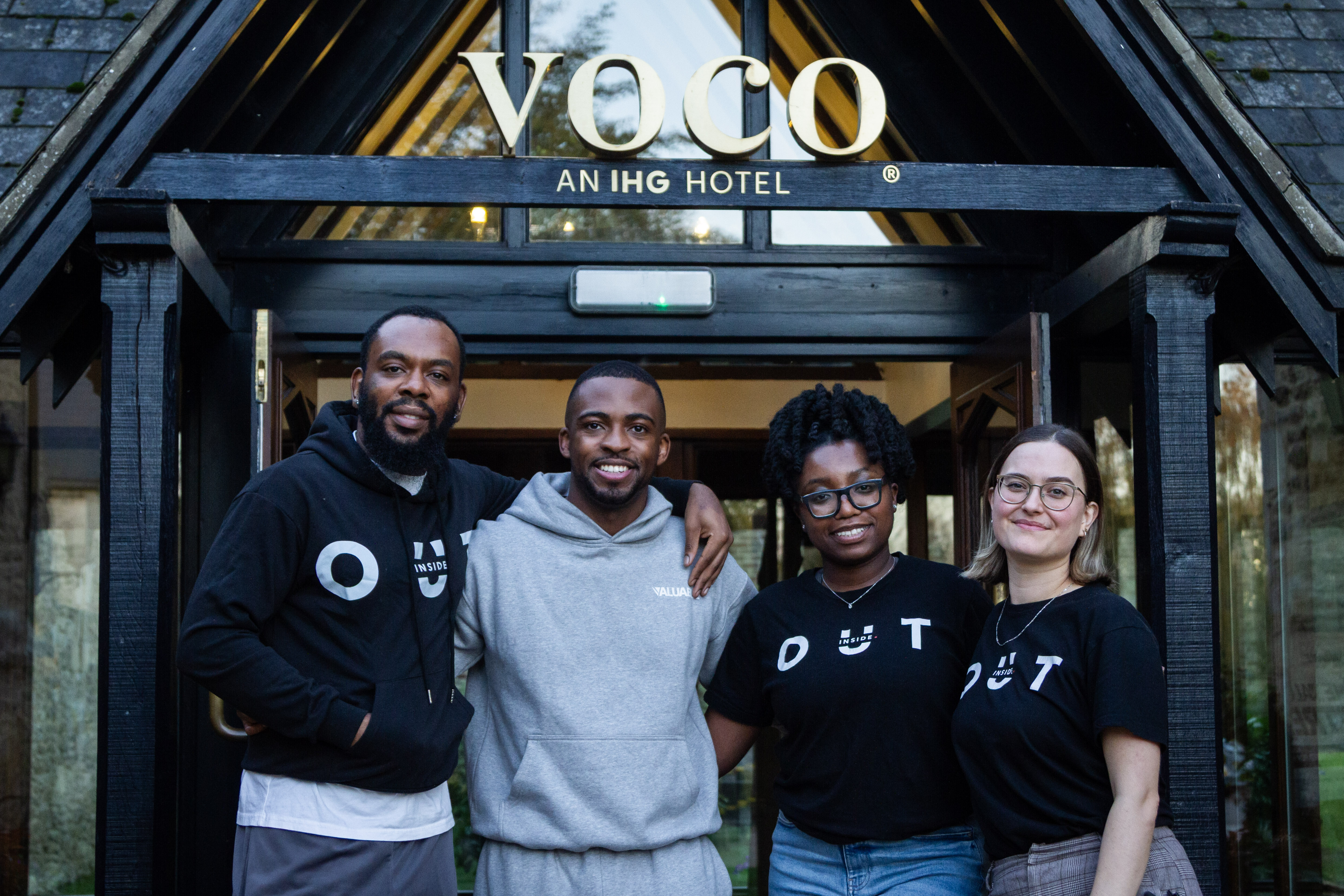 Four people in front of a Voco hotel entrance smiling and posing for photo. 