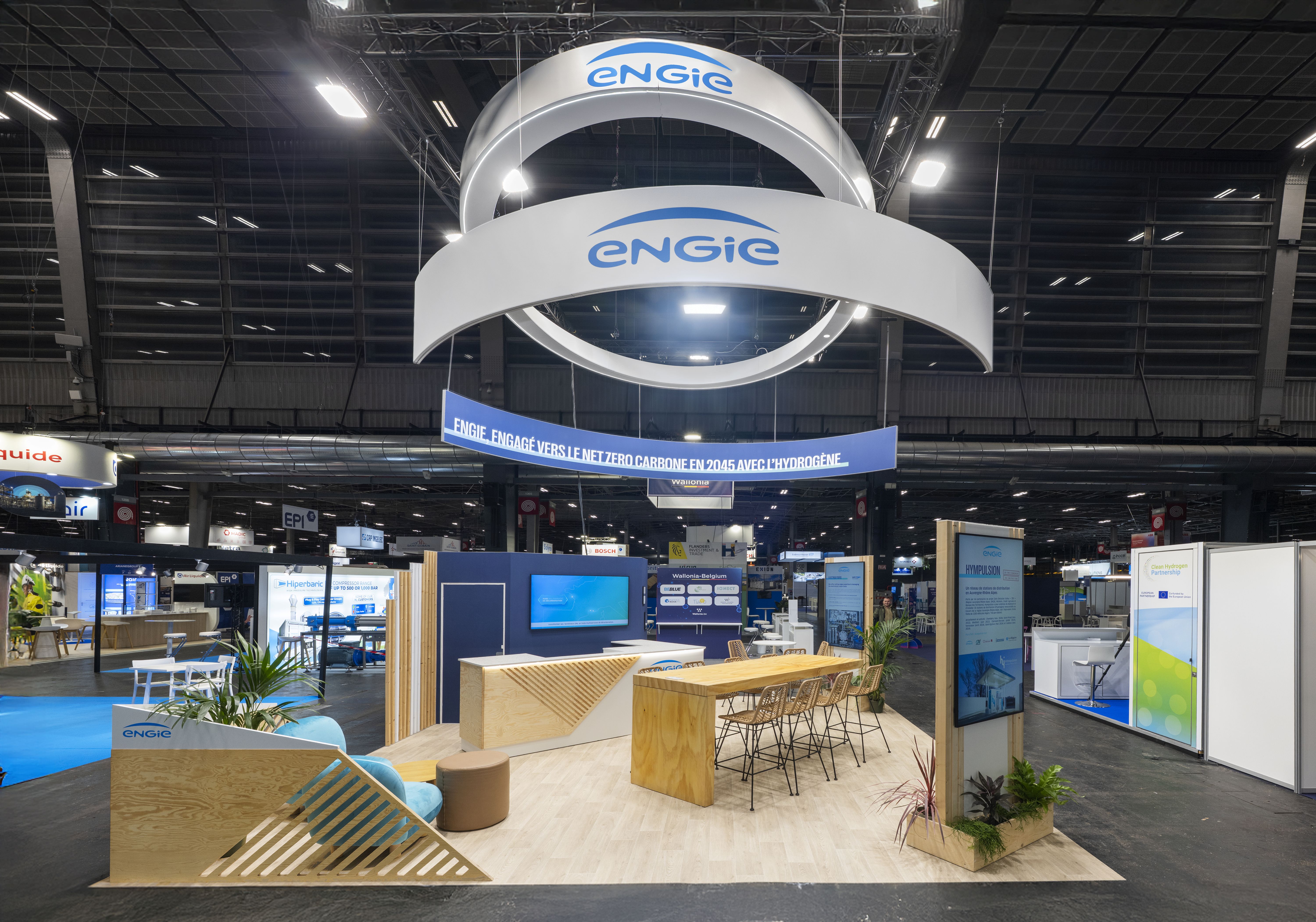 Stand ENGIE Hyvolution Paris 2026 conçu par Expace – vue frontale avec totem lumineux ondulant bleu, logo ENGIE en hauteur, aménagement naturel bois et végétaux et stands produits transition énergétique