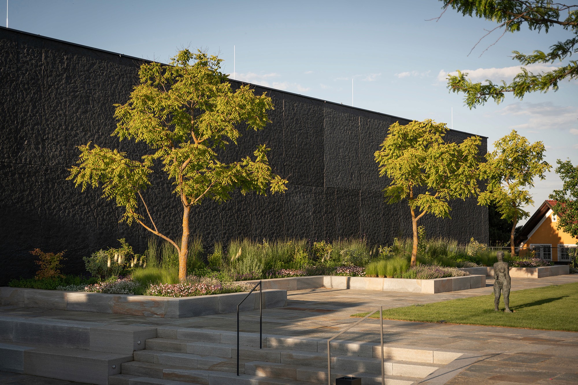 Terrassierte Gartenanlage mit Natursteinmauern, Bäumen und Staudenpflanzungen.