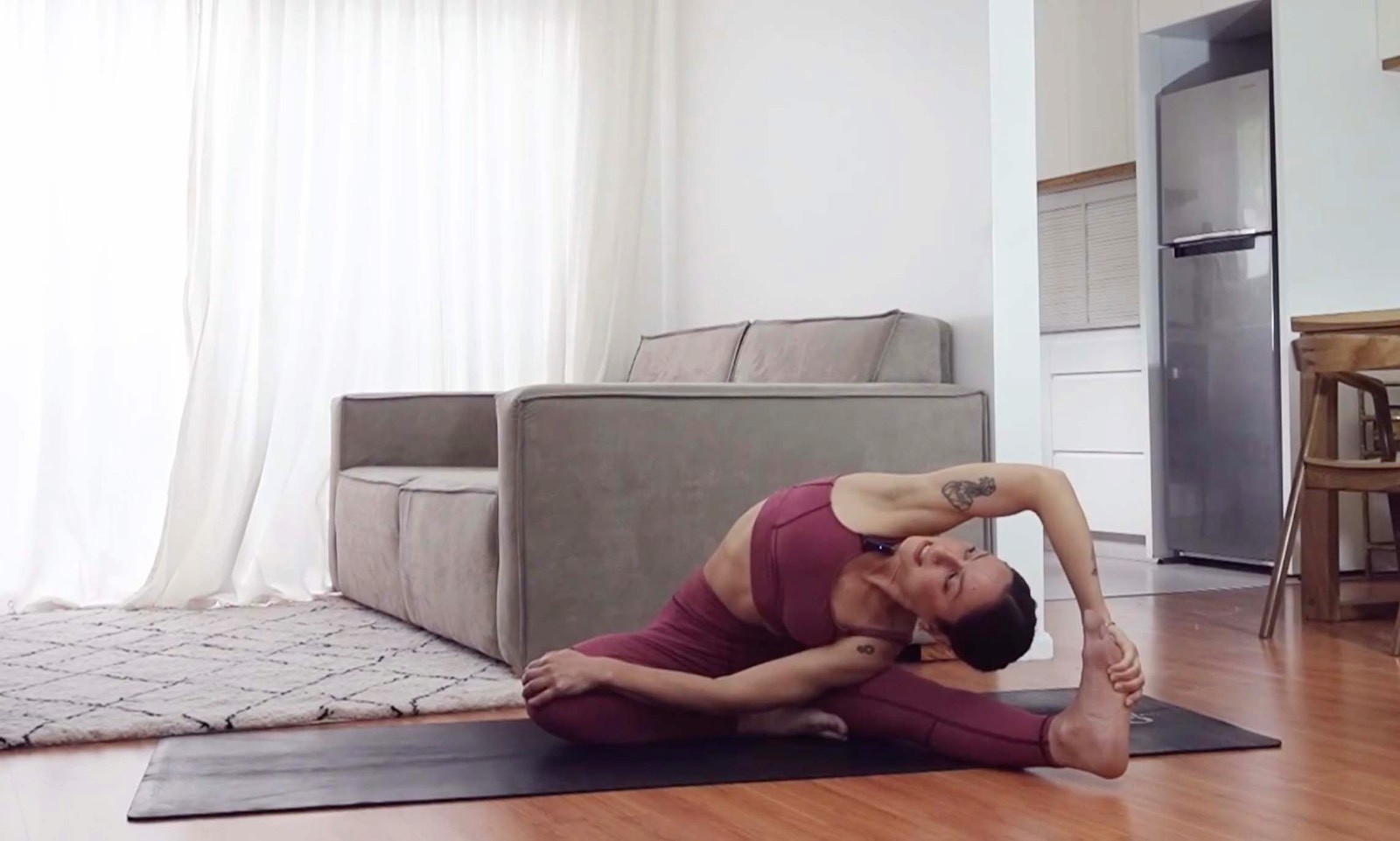 Flavia Siutti practicando una postura de estiramiento lateral sentada sobre una esterilla de yoga.