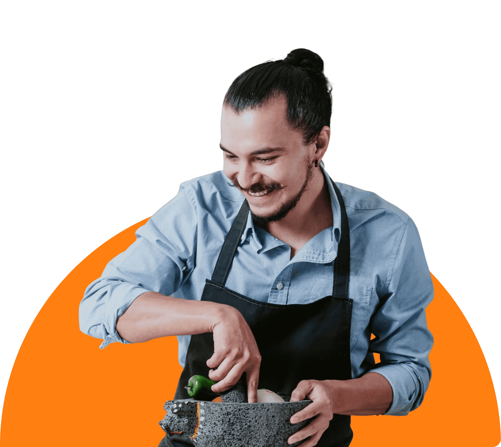 Man in an apron smiles while grinding ingredients with a mortar and pestle