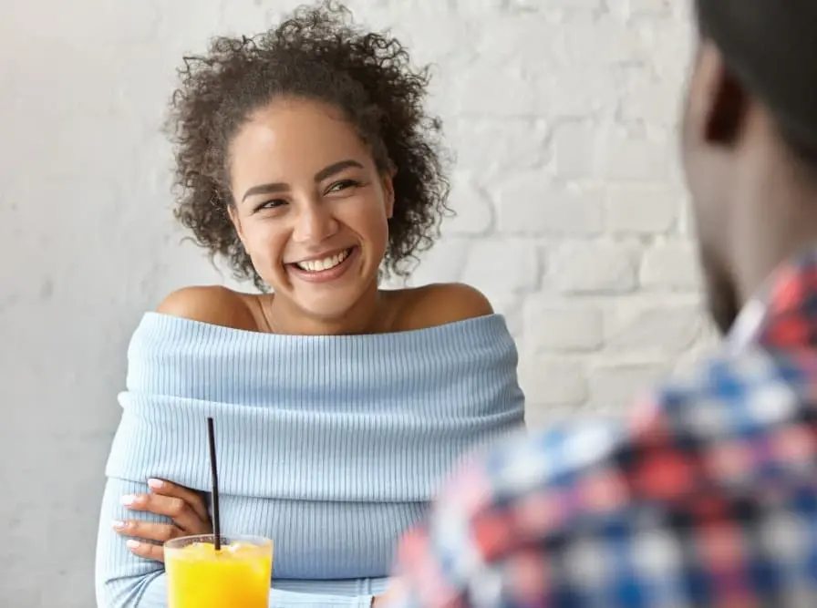 A smiling woman enjoys a friendly conversation over drinks at a café. The bright, relaxed setting conveys comfort and approachability—reflecting the ease and personal connection clients experience when refinancing with Chris Lewis Home Loans.