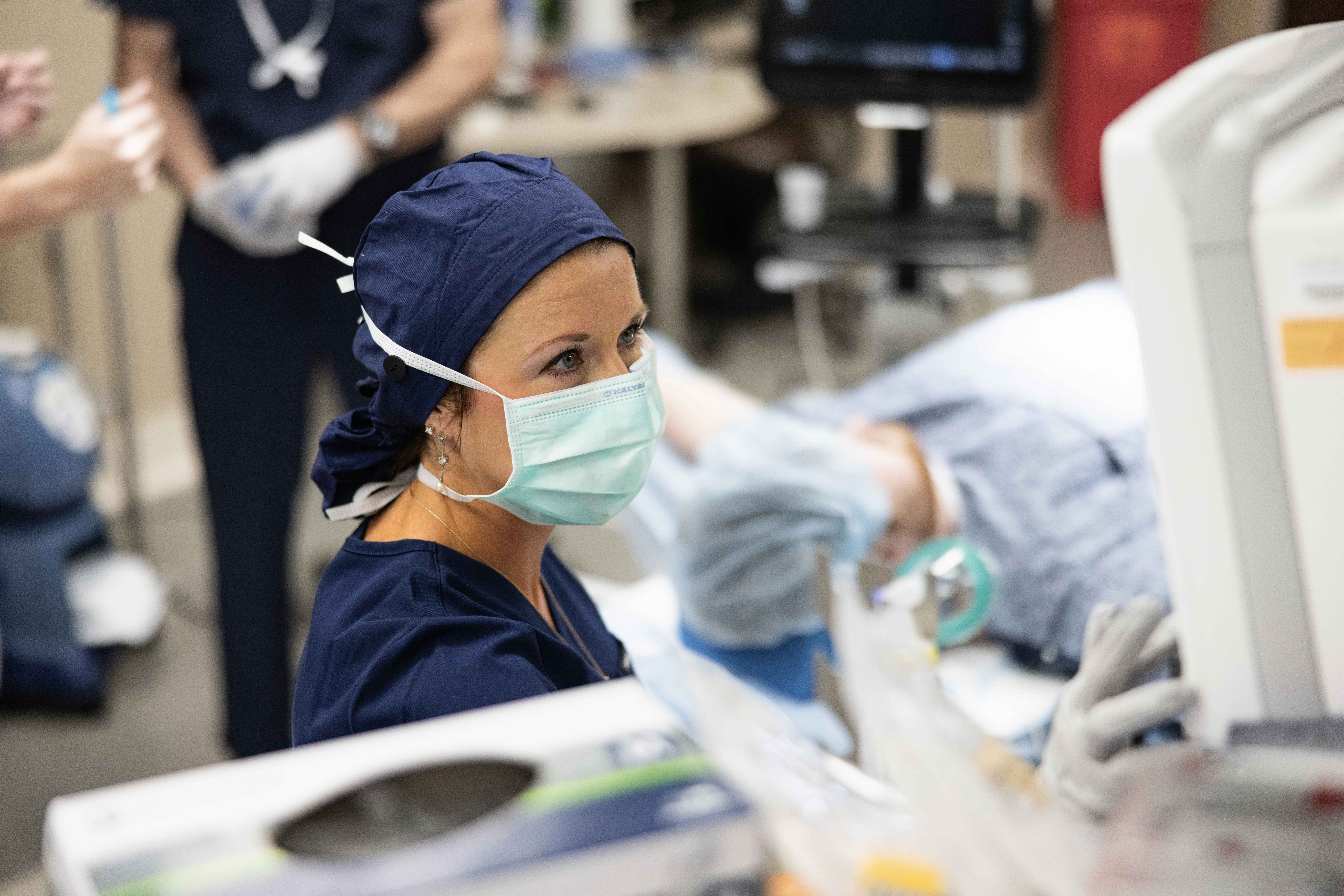 A LifeLinc CRNA in navy scrubs, surgical cap, and mask attends to a patient during a procedure, representing part-time anesthesia provider positions