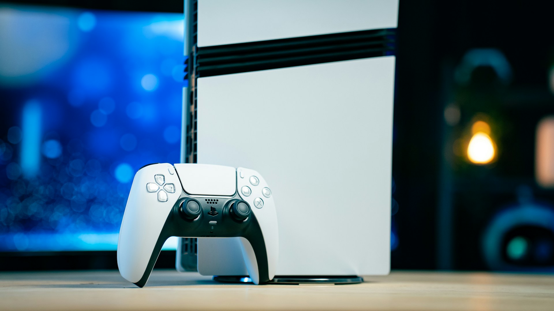 A white PlayStation 5 (PS5) console is standing next to its matching white DualSense controller, with a dark, colorful background.