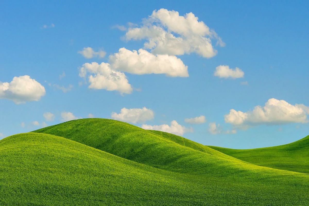 green grass field near green mountains under white clouds during daytime