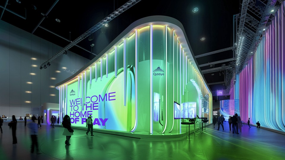 A futuristic exhibition hall features vibrant, multicolored LED lights illuminating the curved walls, with a large sign reading "Welcome to the Home of Play," attracting attendees in the spacious, modern venue.