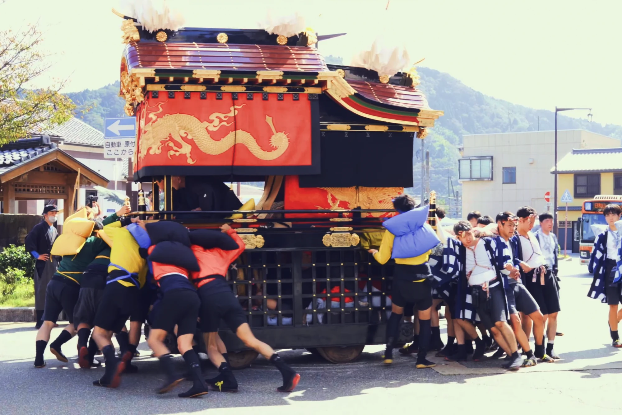 Bearers in happi coats hauling a festival float along a Kinosaki street in daylight.