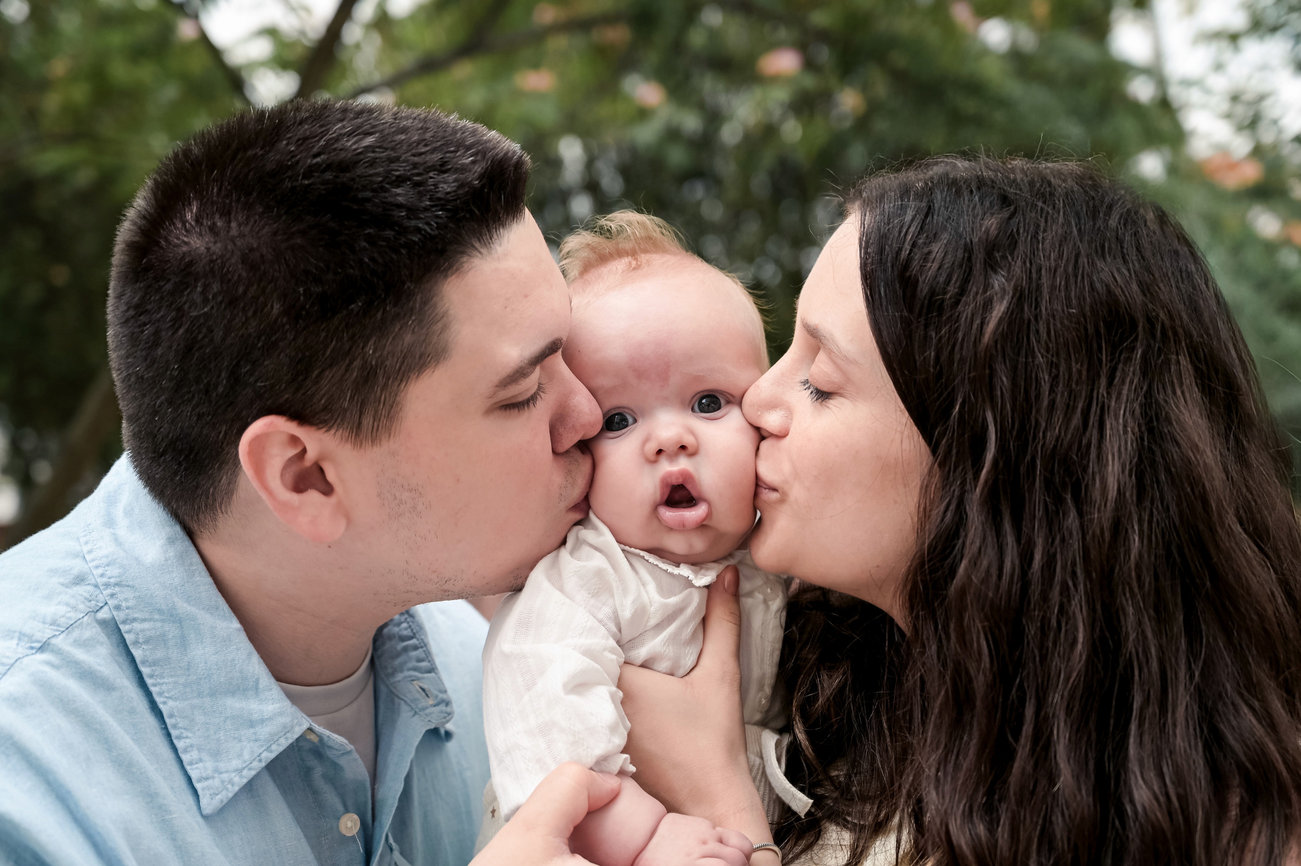 Mama si tatal sărutând bebelușul la botez — moment emoționant surprins în timpul ședinței foto de botez.