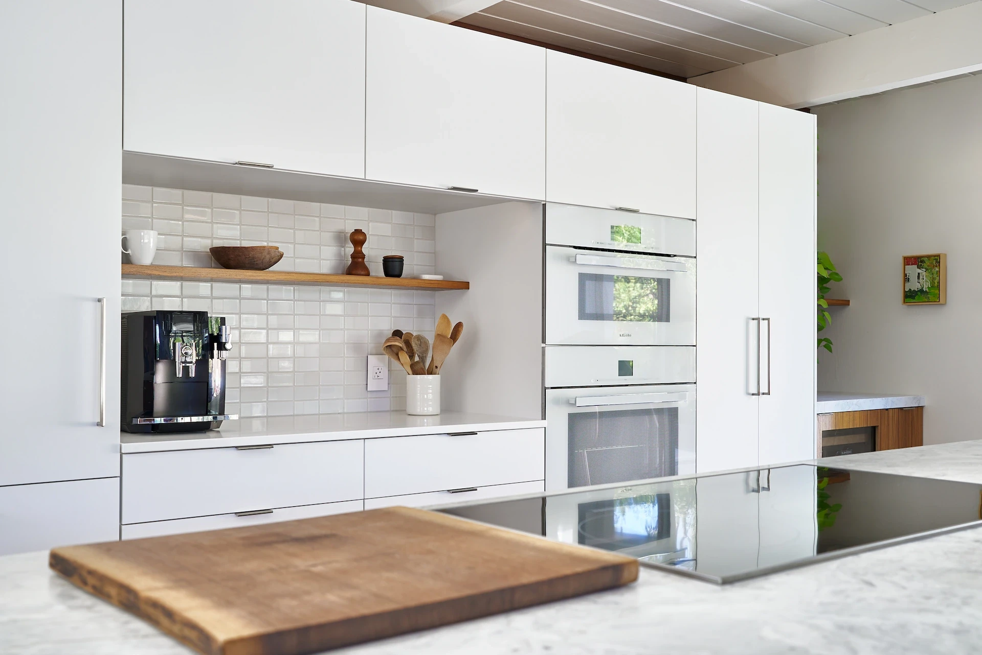 Wide shot of the oven wall from over the kitchen island, featuring the induction range and modern design elements in the Eichler kitchen remodel. Photo by Todd Huge.