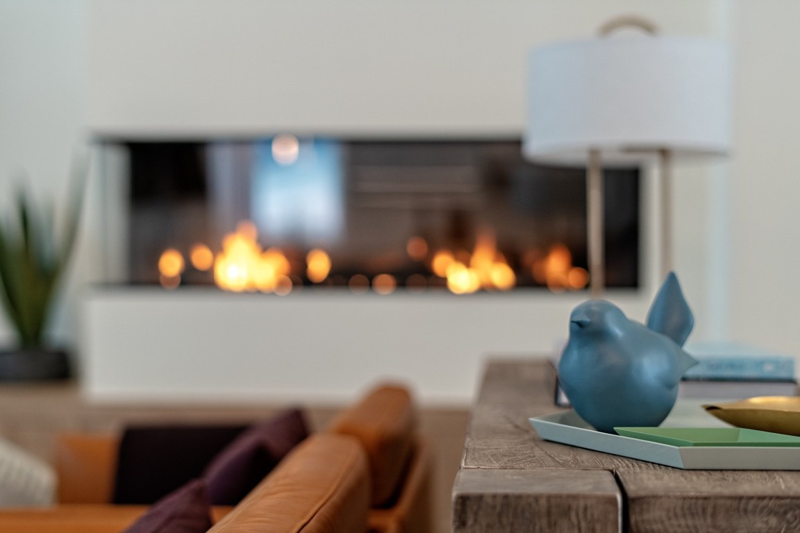 A blue ceramic bird sits on a table in front of a modern living room with a bright gas fireplace.