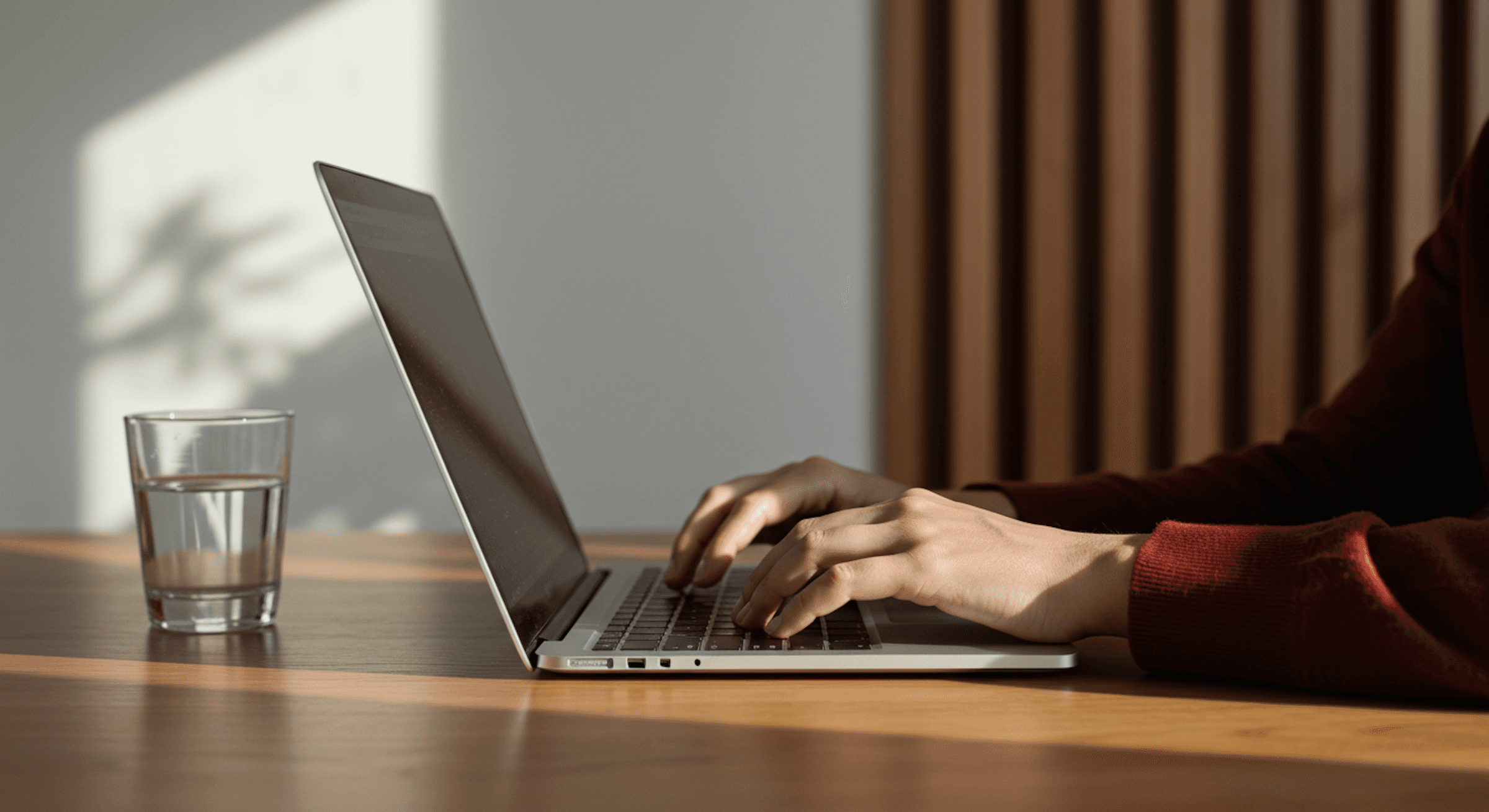 A person in a rust-colored sweater types on a laptop beside a lit candle, creating a cozy and focused atmosphere.